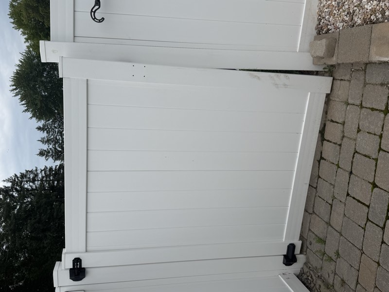 A gate post leaning out of plumb, propped upright by a concrete block, with unused screw holes above the hinge.