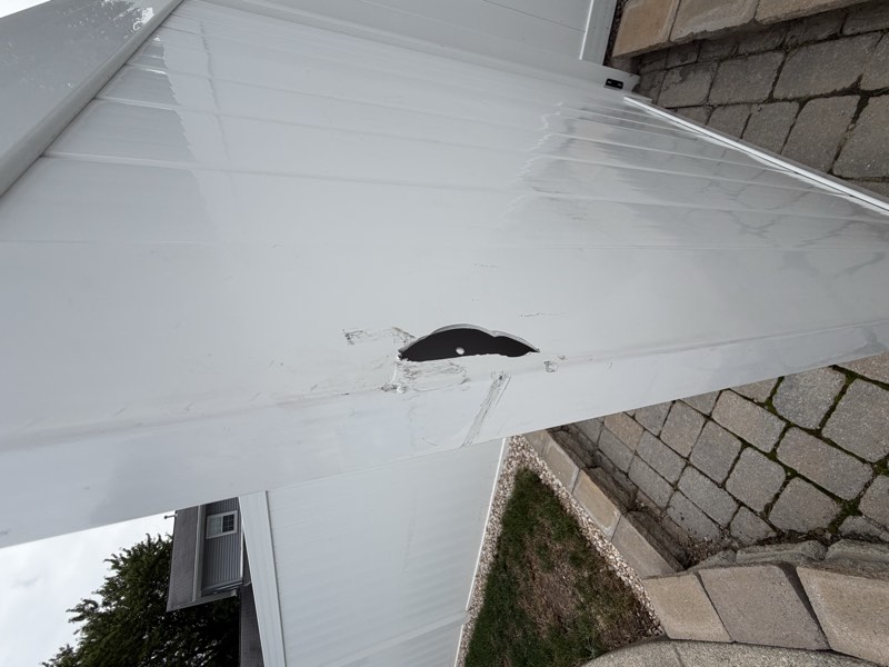 A hole punched clean through a vinyl fence panel with caulk residue around it.
