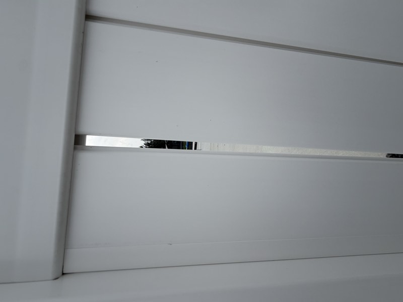 An open vertical gap between fence panel boards with the yard visible through it.