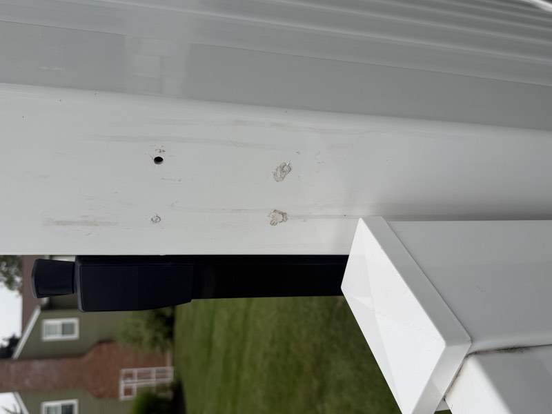 An open drilled hole and two caulk plugs on a gate post beside black gate hardware.