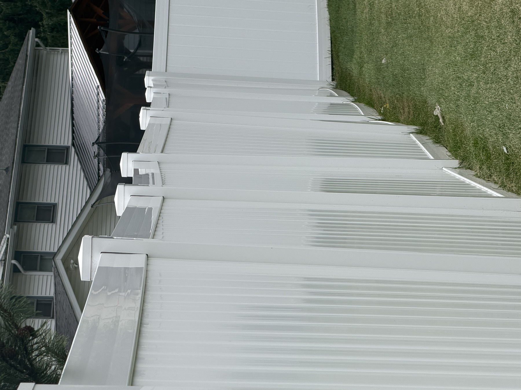 A run of white vinyl fence posts, each leaning at a different angle, with the top rail line sagging between them and the post caps sitting at staggered heights.